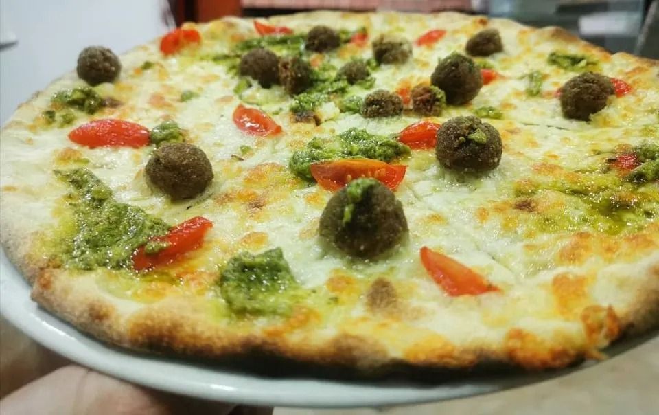 Pizza topped with green pesto, cherry tomatoes, and meatballs on a white plate