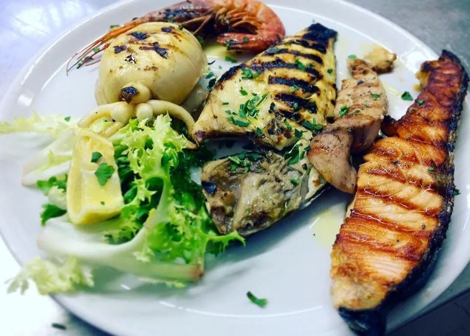 Piatto di frutti di mare grigliati con gamberi, pesce, broccoli e banana grigliata su un piatto bianco.