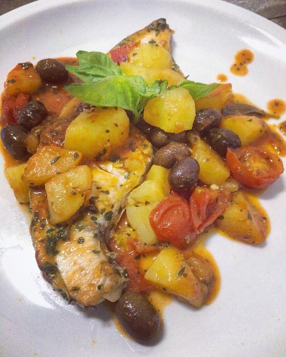 Pesce servito con patate arrosto, fagioli neri, pomodorini e guarnizione di basilico.