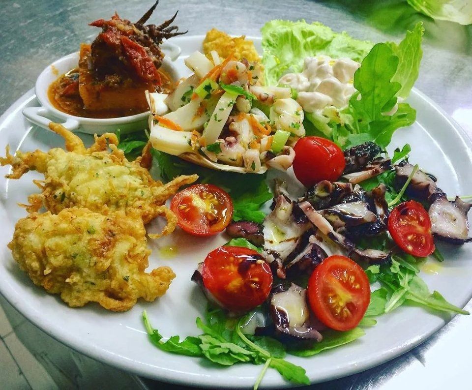 Antipasti misti e insalata su un piatto bianco con verdure, pomodorini e salsa cremosa.