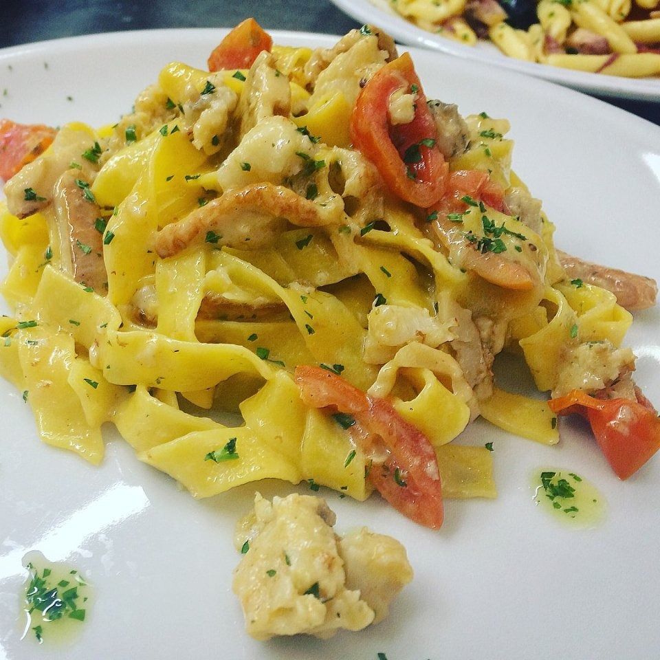 Pasta con salsa cremosa, erbe aromatiche e peperone rosso su un piatto bianco.