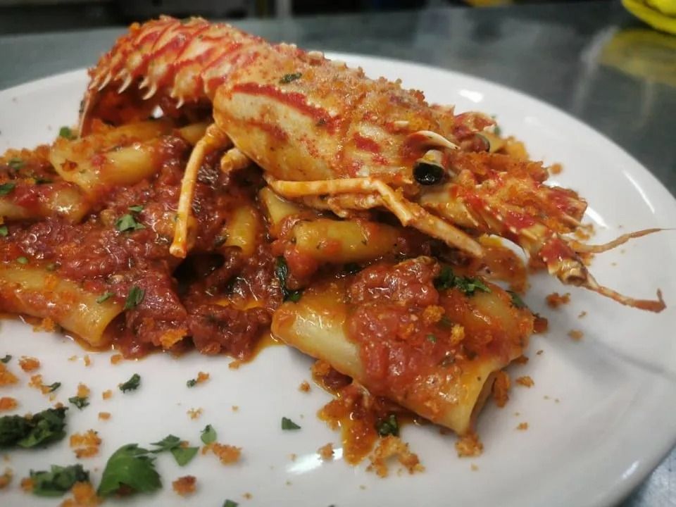 Aragosta e pasta al sugo di pomodoro su un piatto bianco con erbe aromatiche tritate.