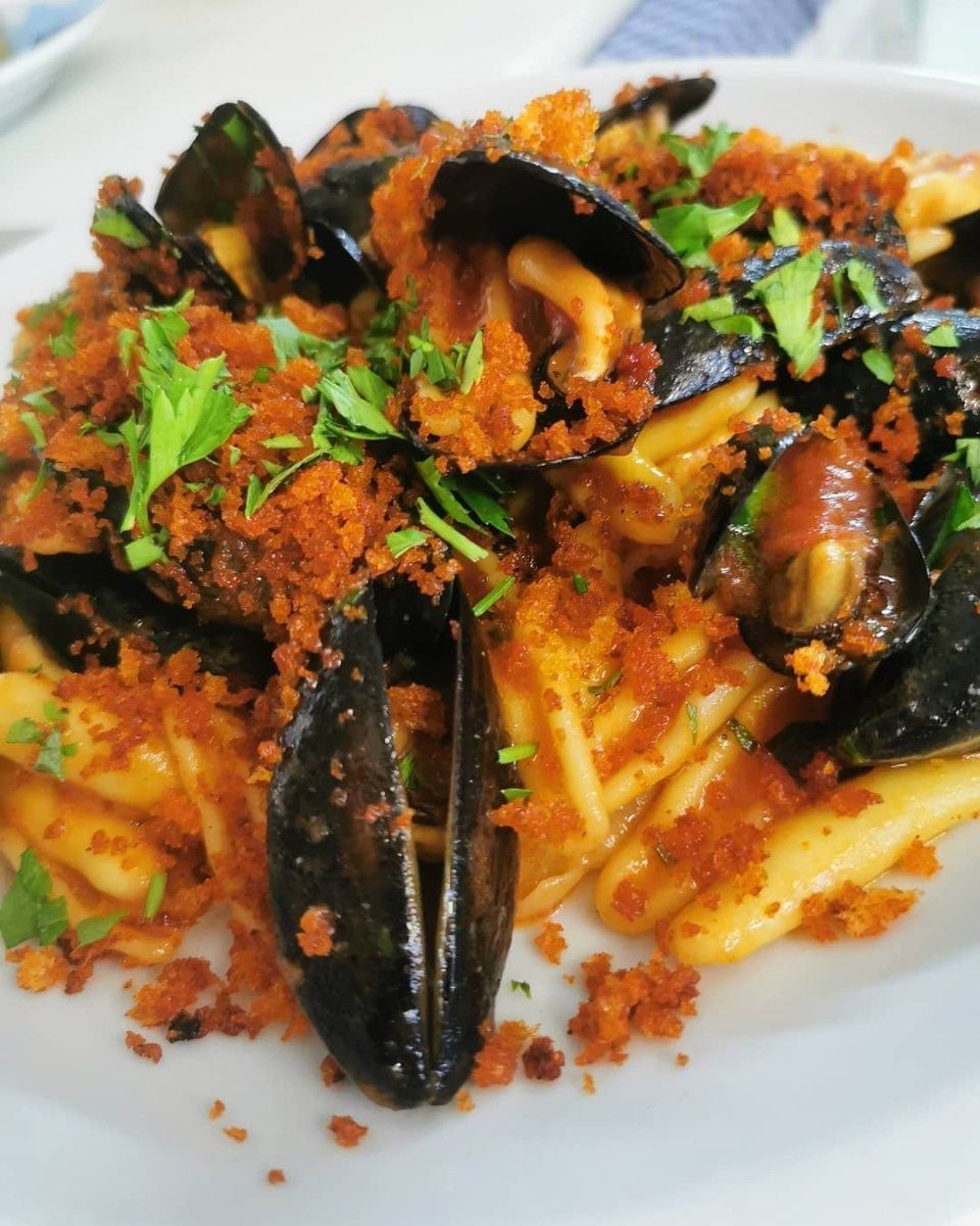 Cozze e patatine fritte condite con salsa rossa e prezzemolo fresco su un piatto bianco.