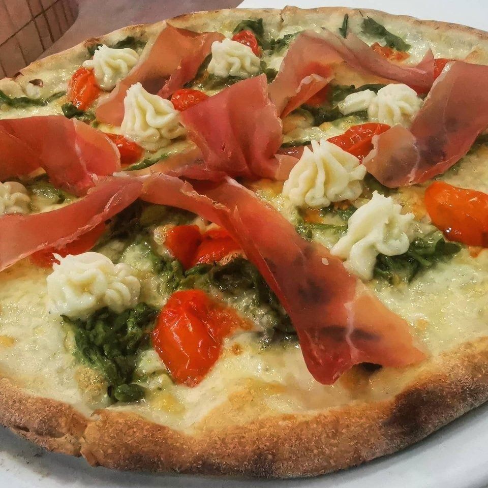 Pizza topped with prosciutto, cherry tomatoes, basil, and cream on a white plate