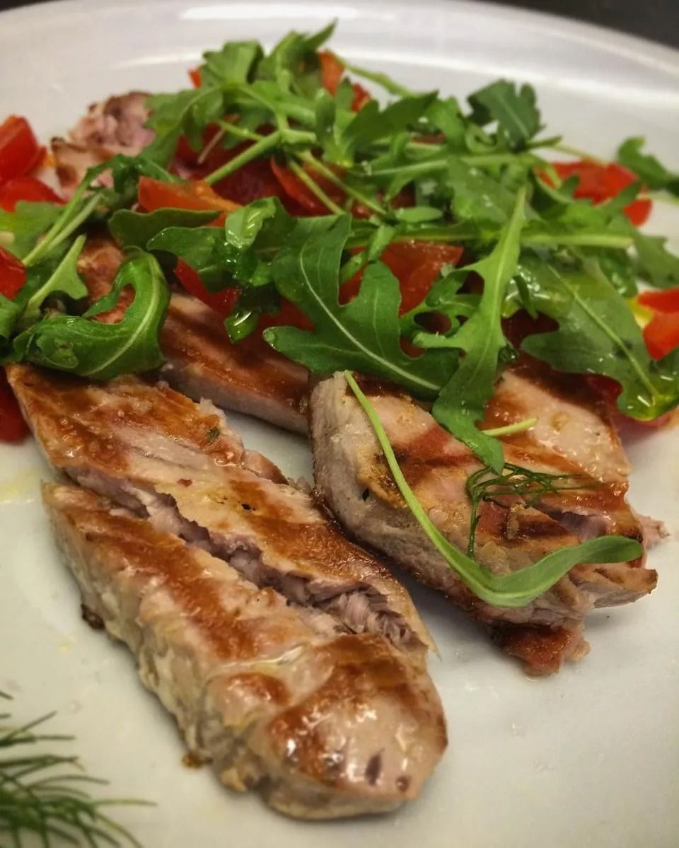 Filetti di pesce grigliati con rucola su un piatto bianco e pezzetti di peperone rosso.