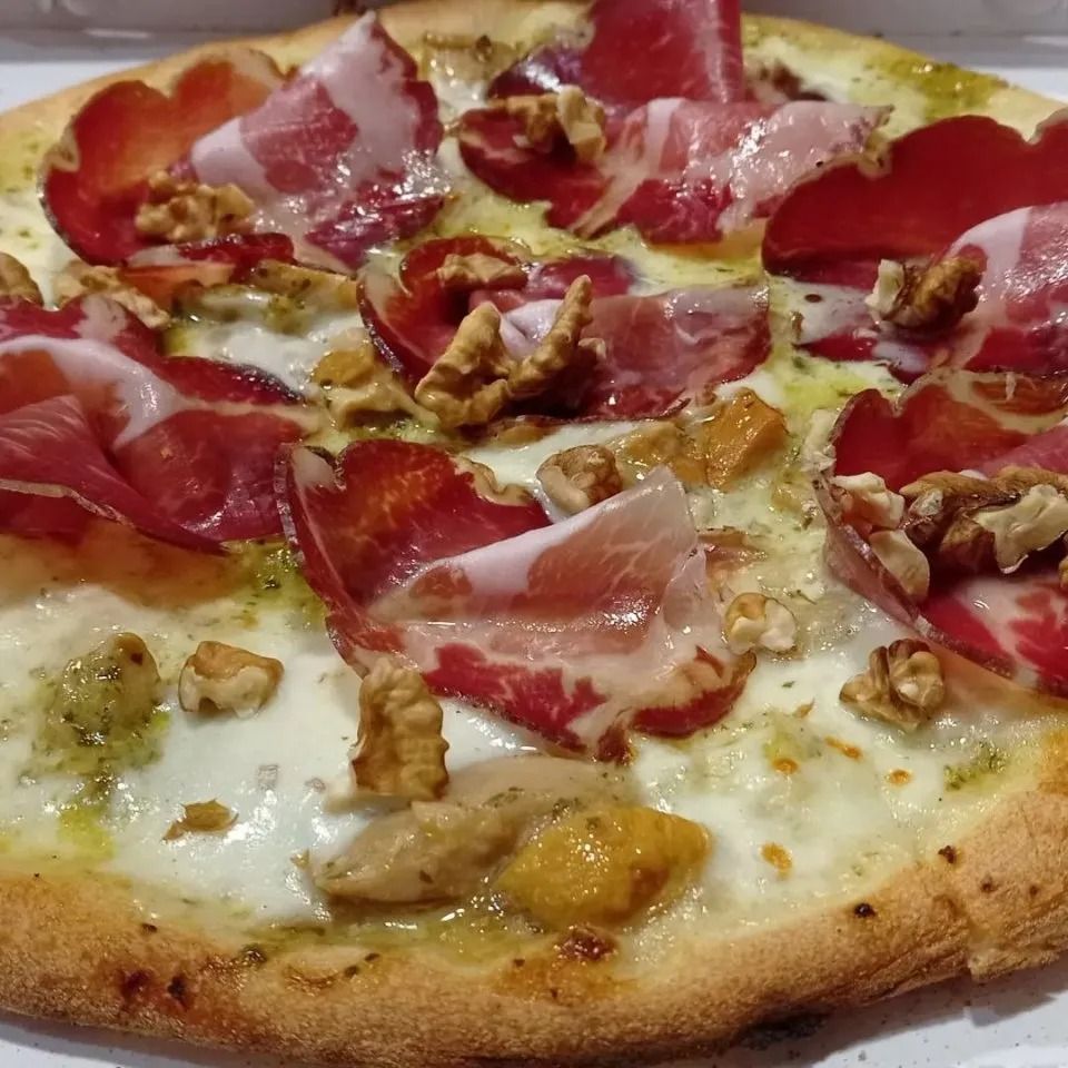 Close-up of a pizza topped with prosciutto, walnuts, and melted cheese on a golden crust
