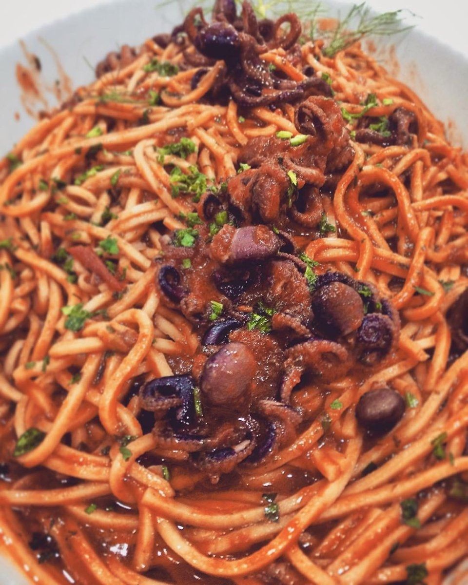 Spaghetti conditi con salsa di pomodoro, funghi ed erbe aromatiche su un piatto bianco.