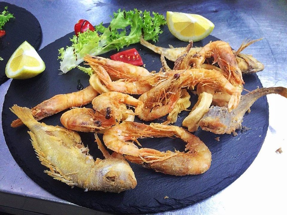 Piatto di gamberi e pesce fritti con spicchi di limone e verdure su un piatto scuro