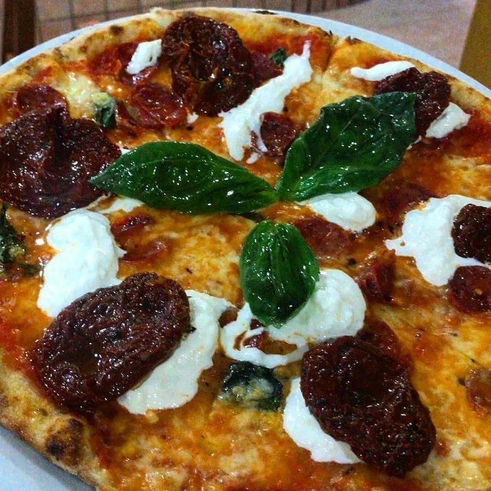 Close-up of a pizza topped with basil leaves, dollops of white cheese, and sun-dried tomatoes