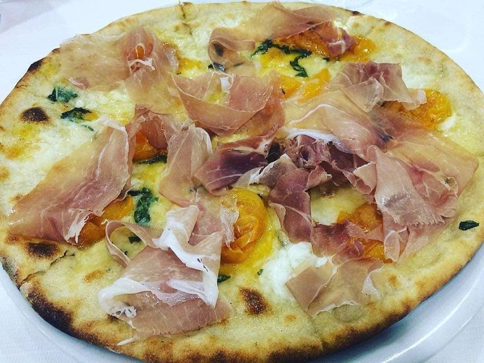 Pizza topped with prosciutto and melted cheese on a white plate
