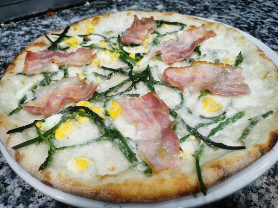 White pizza with ham, green herbs, and melted cheese on a plate