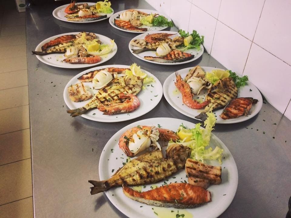 Piatti di pesce grigliato e contorni disposti sul bancone della cucina, pronti per essere serviti.