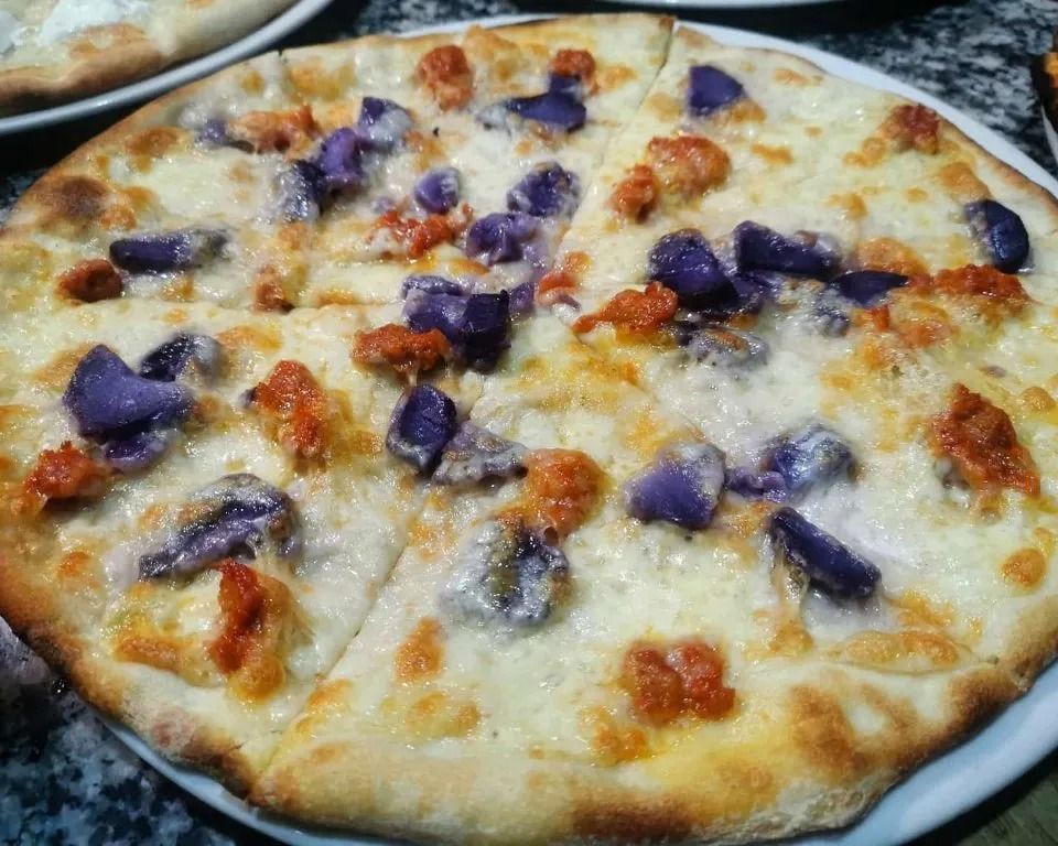 Cheesy pizza topped with purple and orange pieces on a white plate