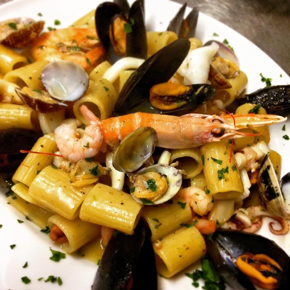 Pasta ai frutti di mare con gamberi, cozze e vongole in una ciotola bianca, guarnita con erbe aromatiche.