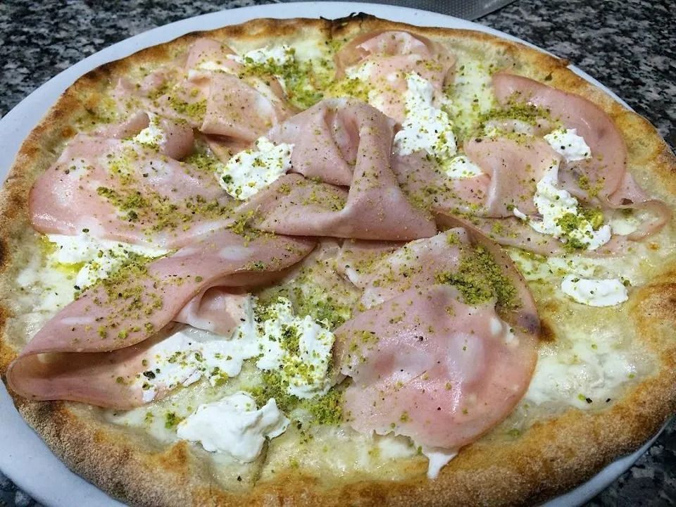Pizza topped with ham, dollops of cheese, and herbs on a white plate