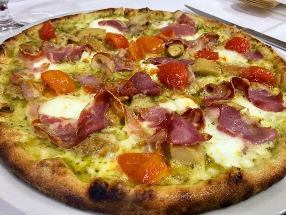 A pizza topped with melted cheese, prosciutto, tomatoes, and herbs on a white plate
