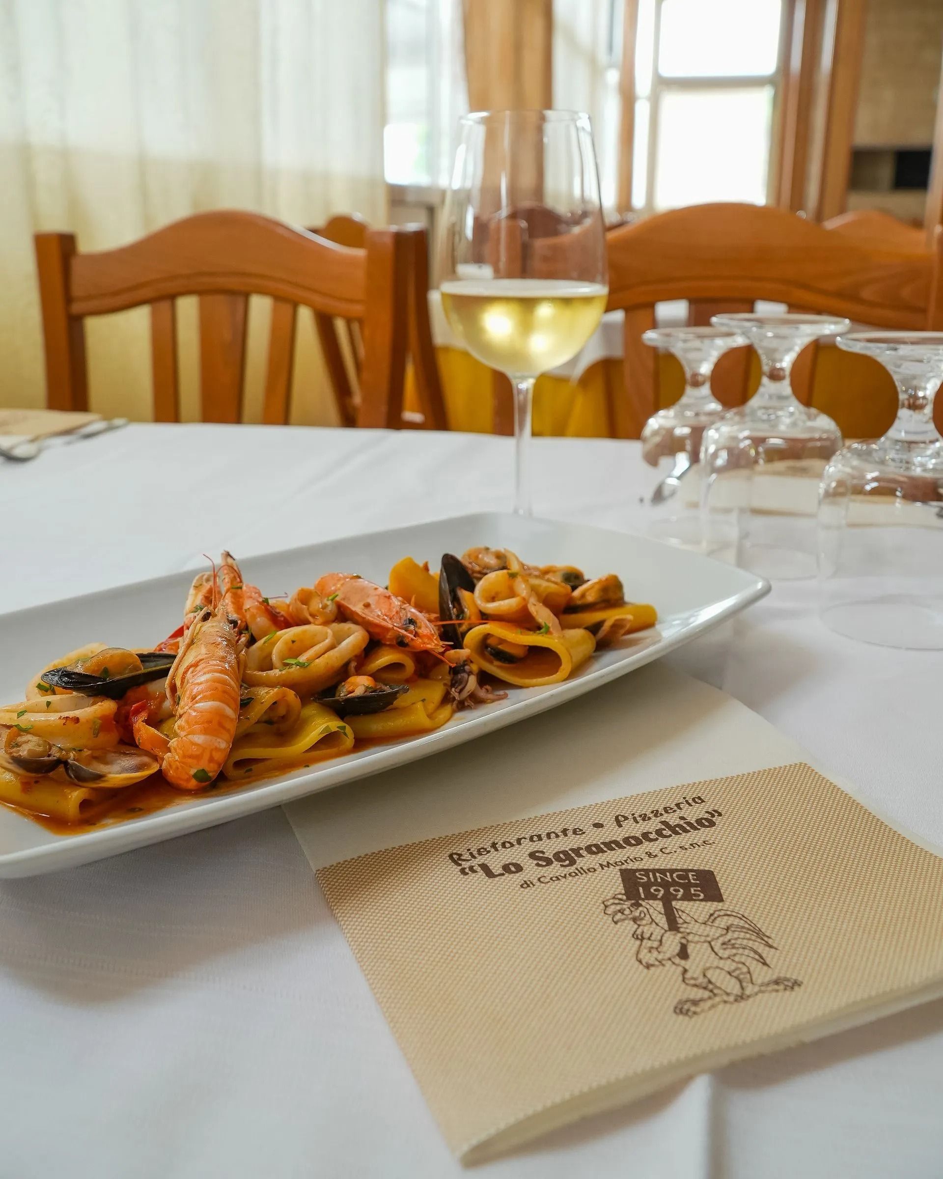 Pasta ai frutti di mare su una tovaglia bianca con un bicchiere di vino bianco in un ristorante luminoso.