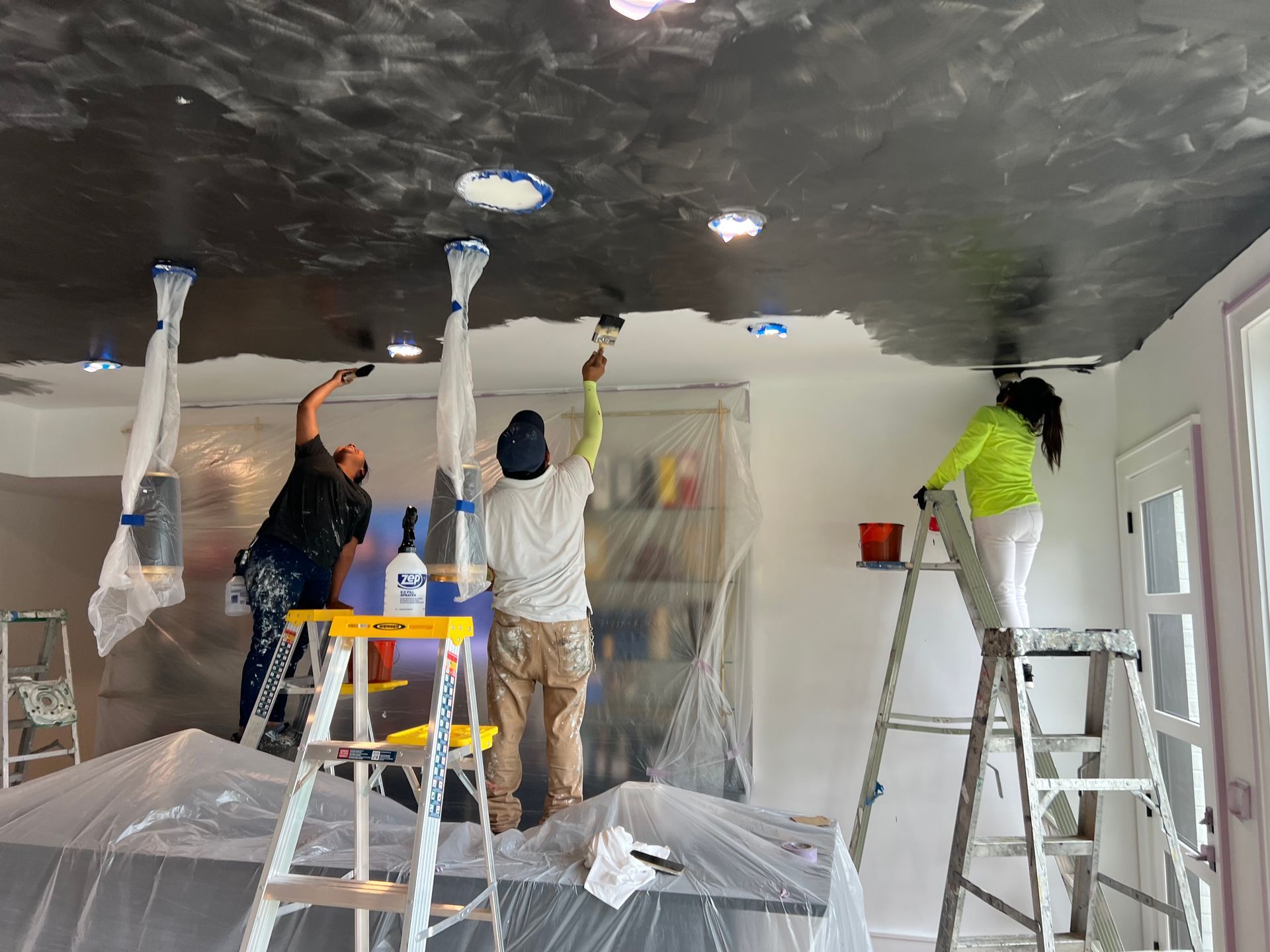 A group of people are painting the ceiling of a room.