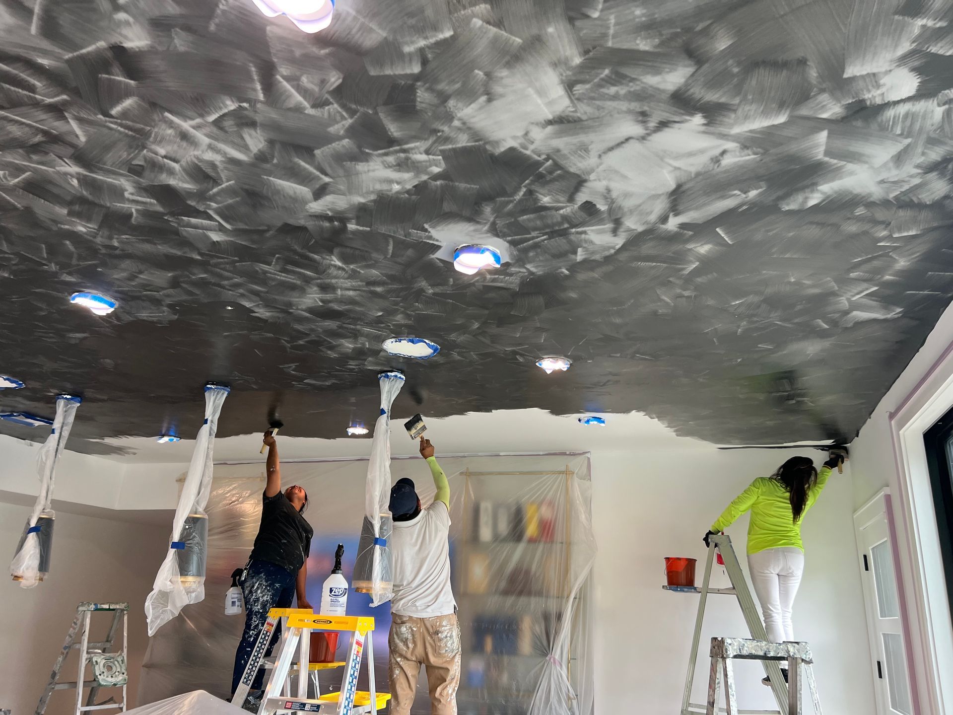 A group of people are painting a ceiling in a room.