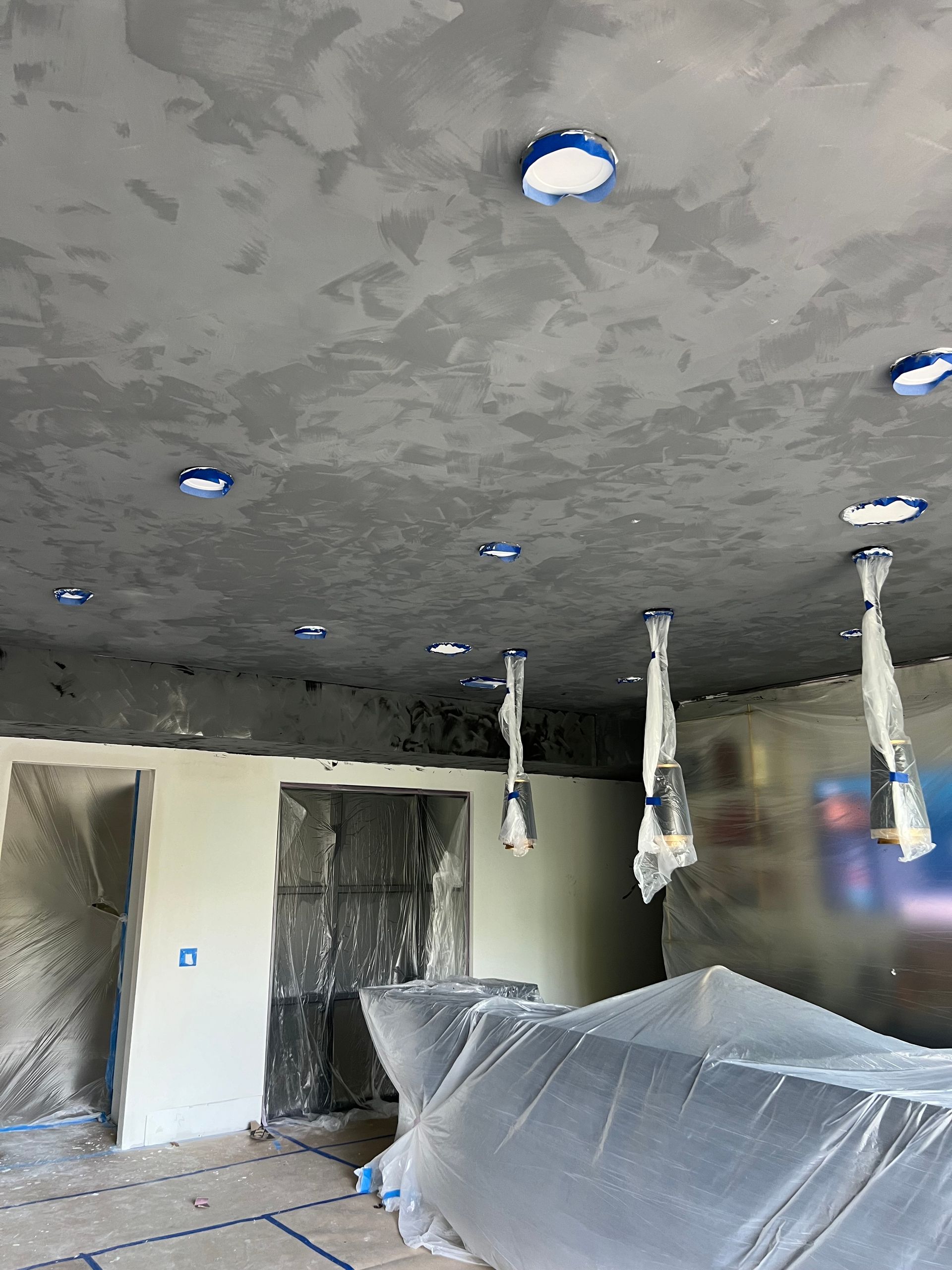 A room with a ceiling that is being painted and covered in plastic.