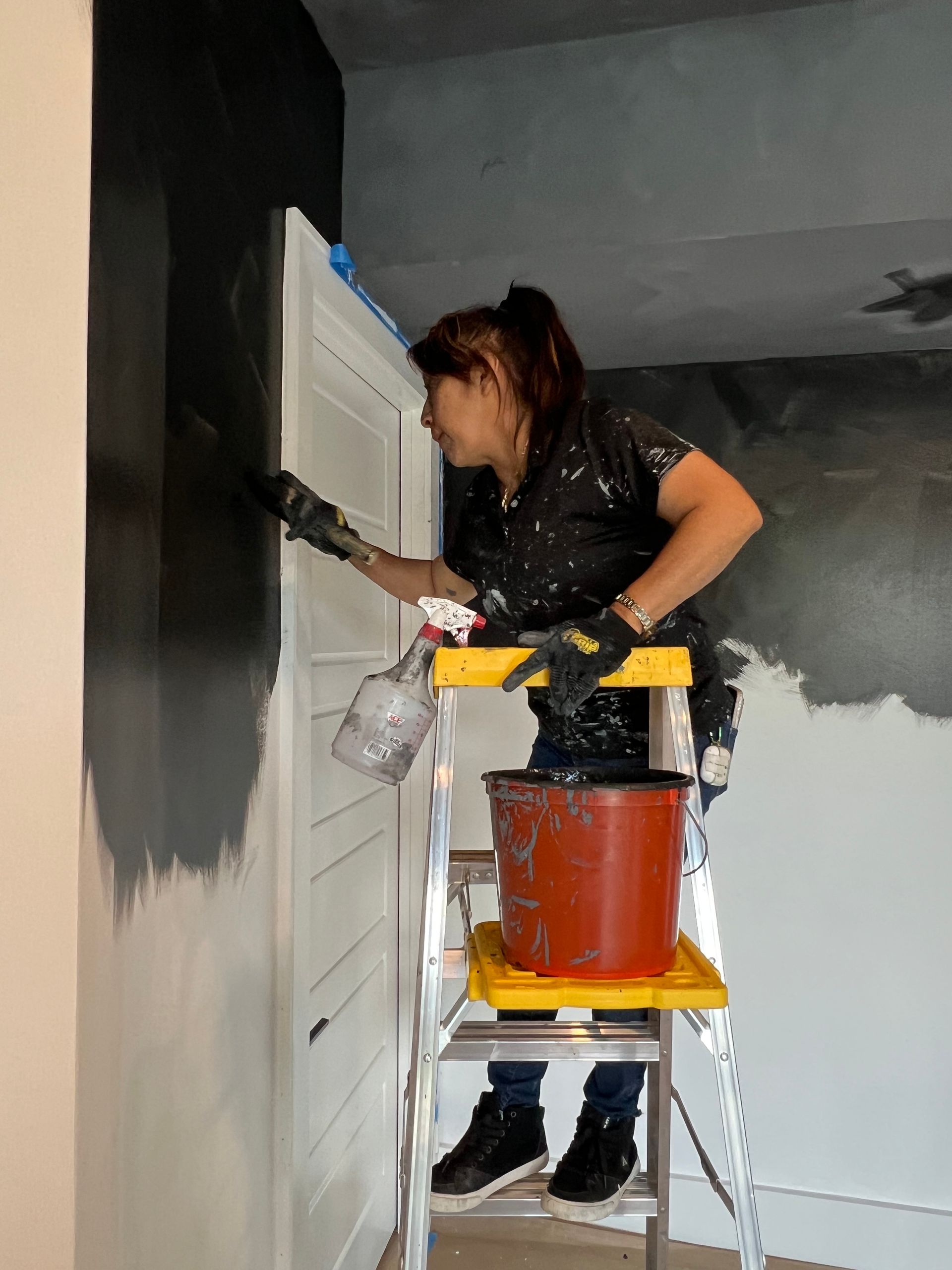 A woman is sitting on a ladder painting a wall
