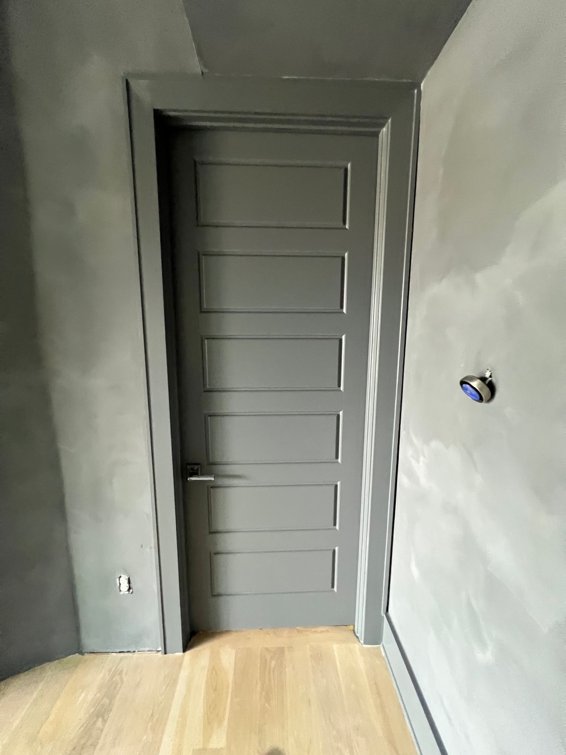 A gray door is in a room with a wooden floor.