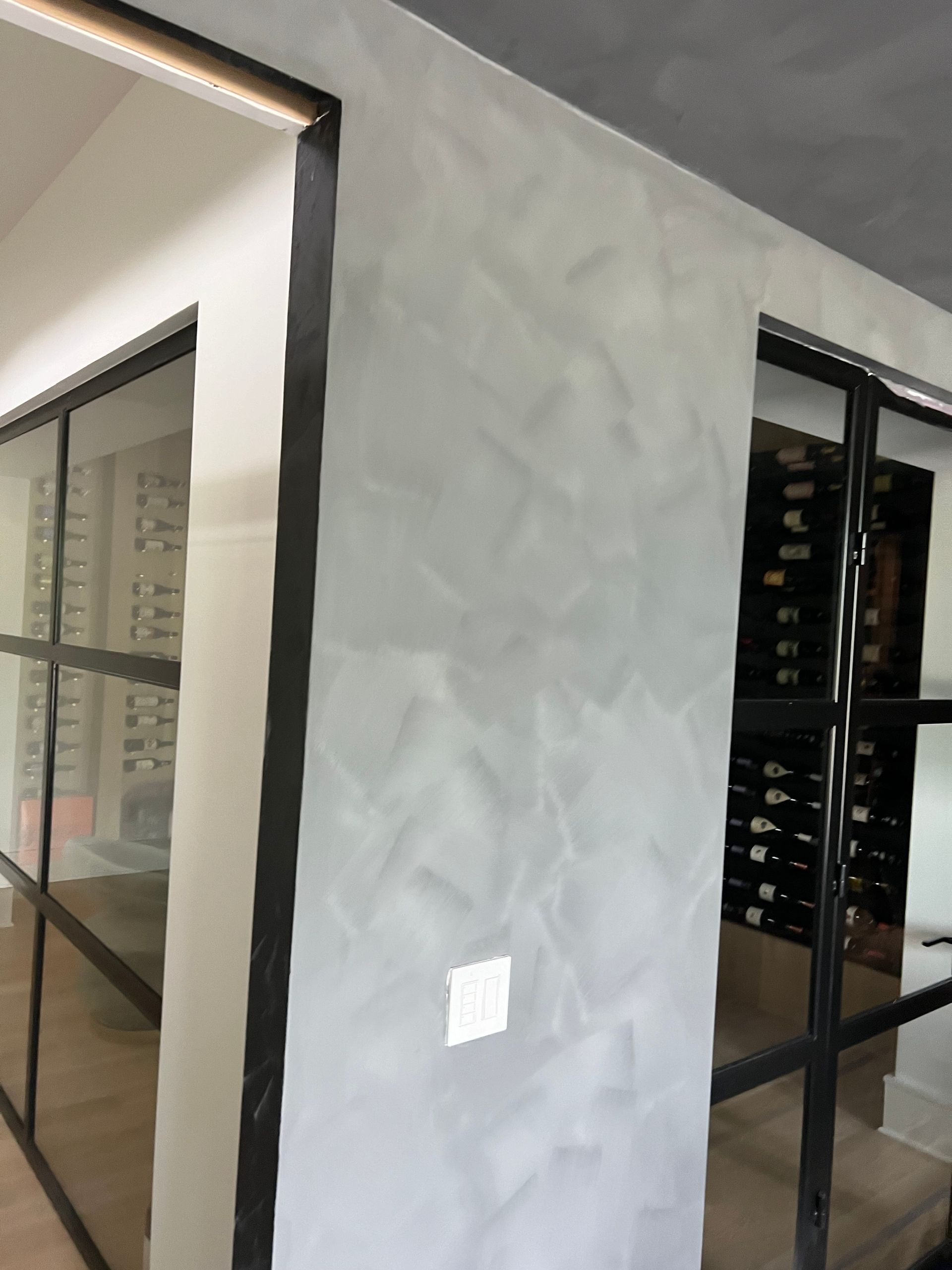 A room with a lot of windows and a wine cellar in the background.