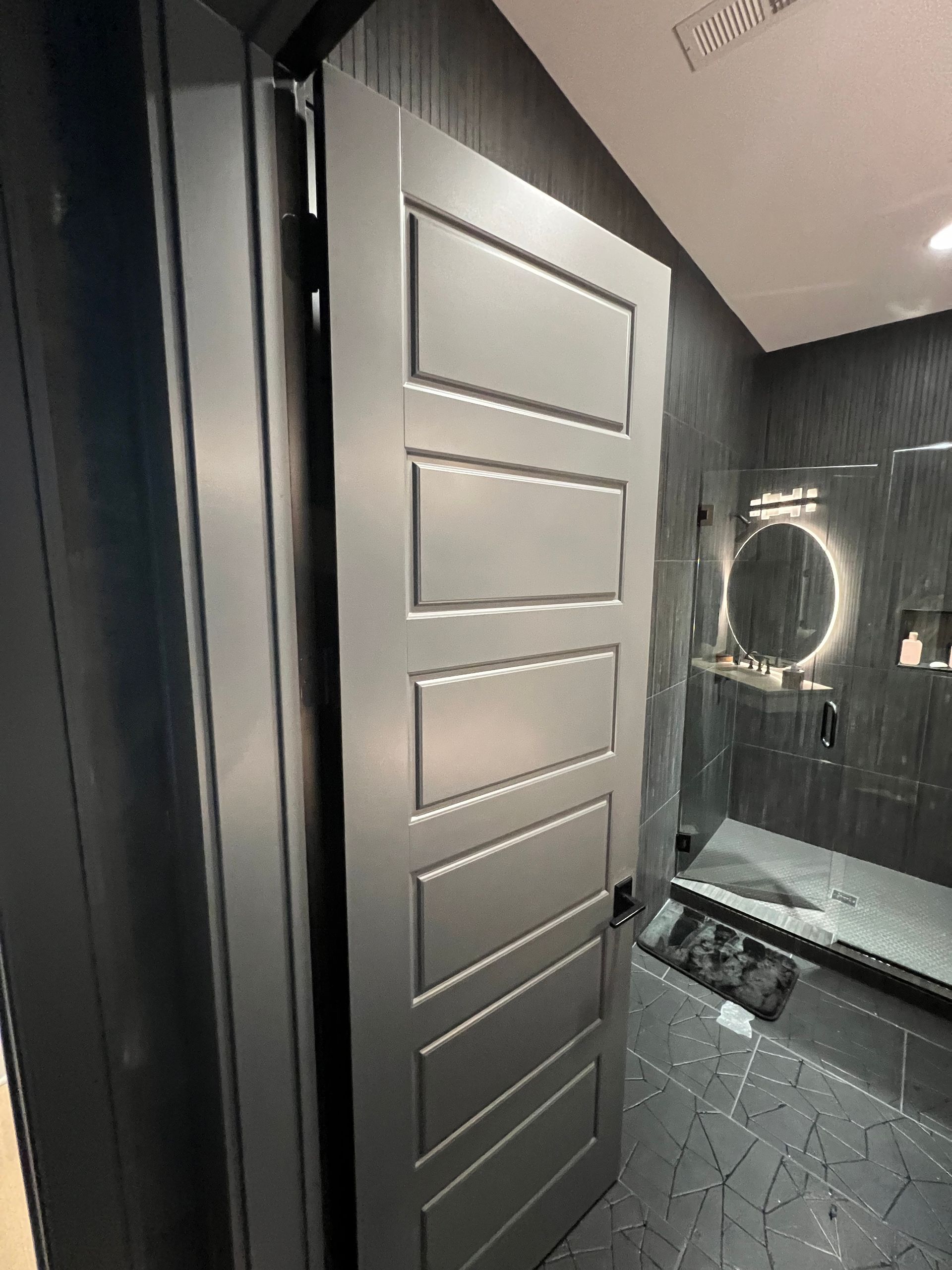 A bathroom with a gray door and a shower stall.