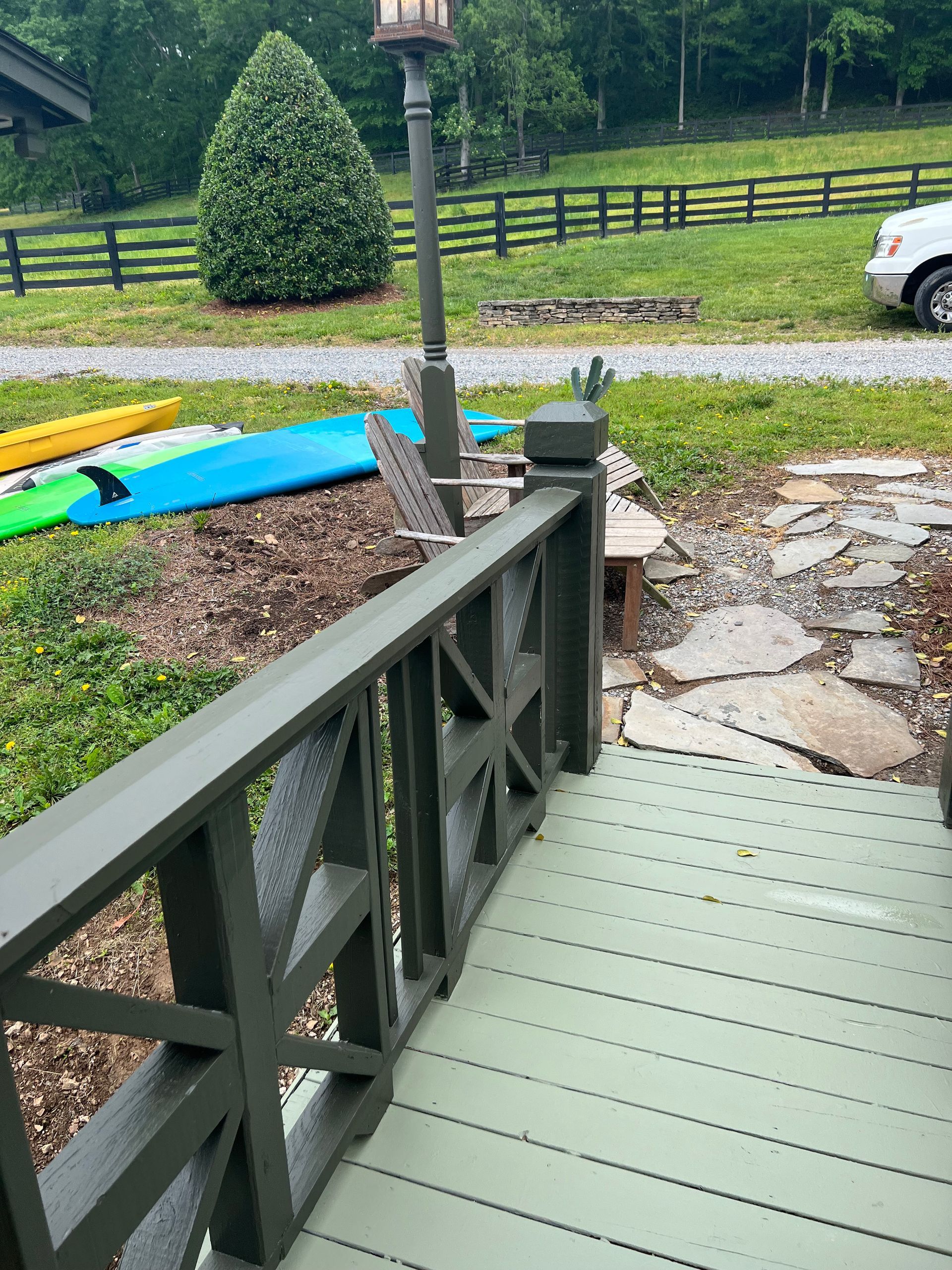 A green deck with a fence and a car parked in the background