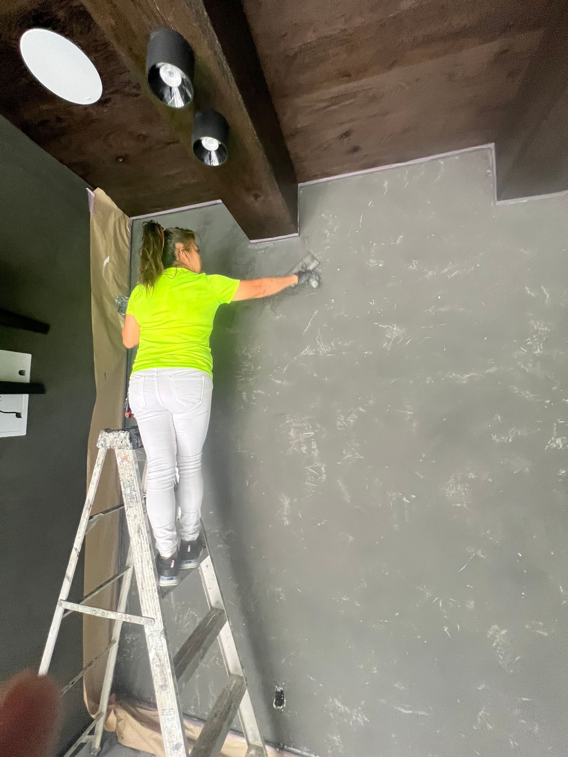 A woman is standing on a ladder painting a wall.