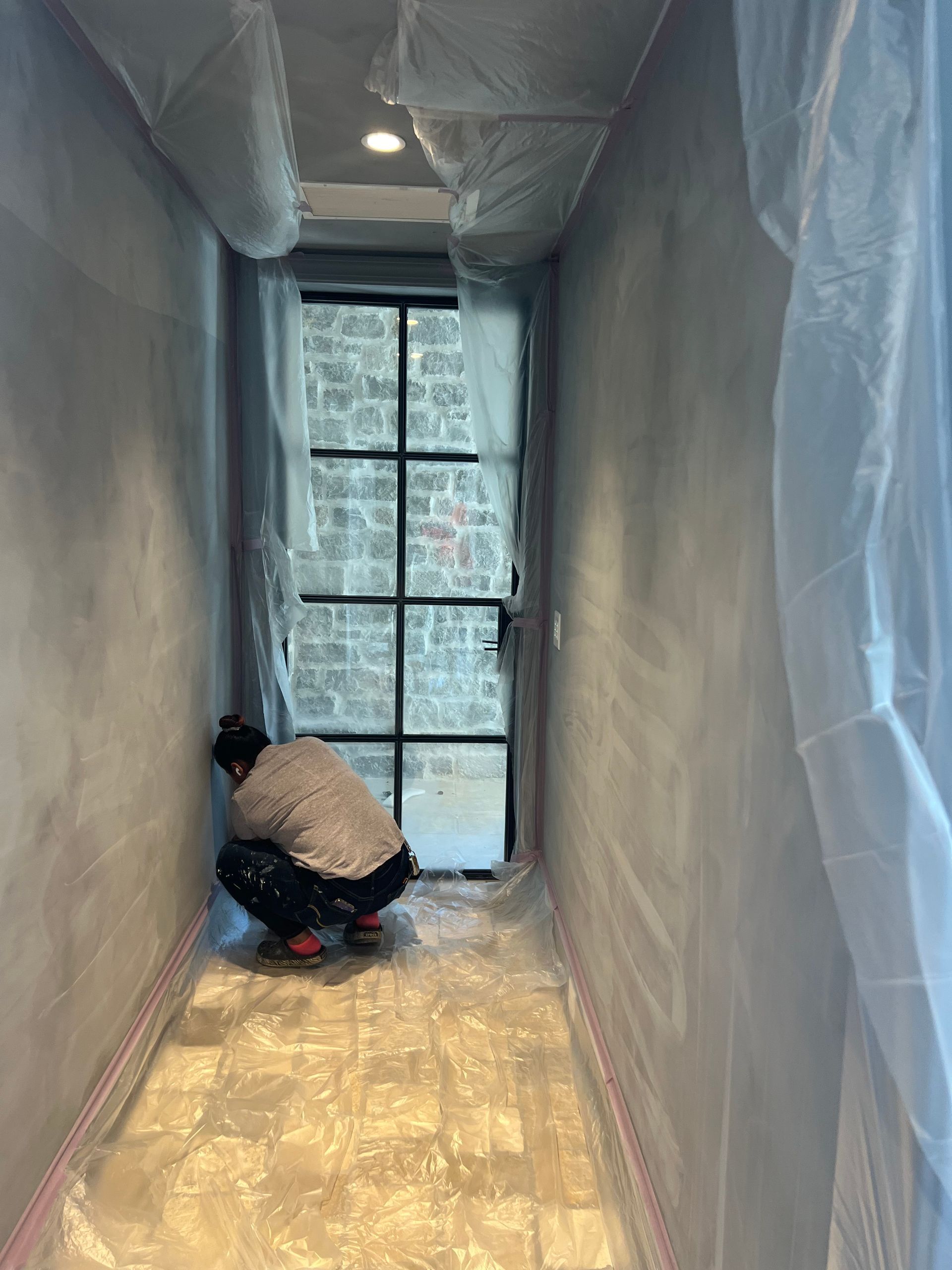 A man is kneeling down in a hallway covered in plastic.