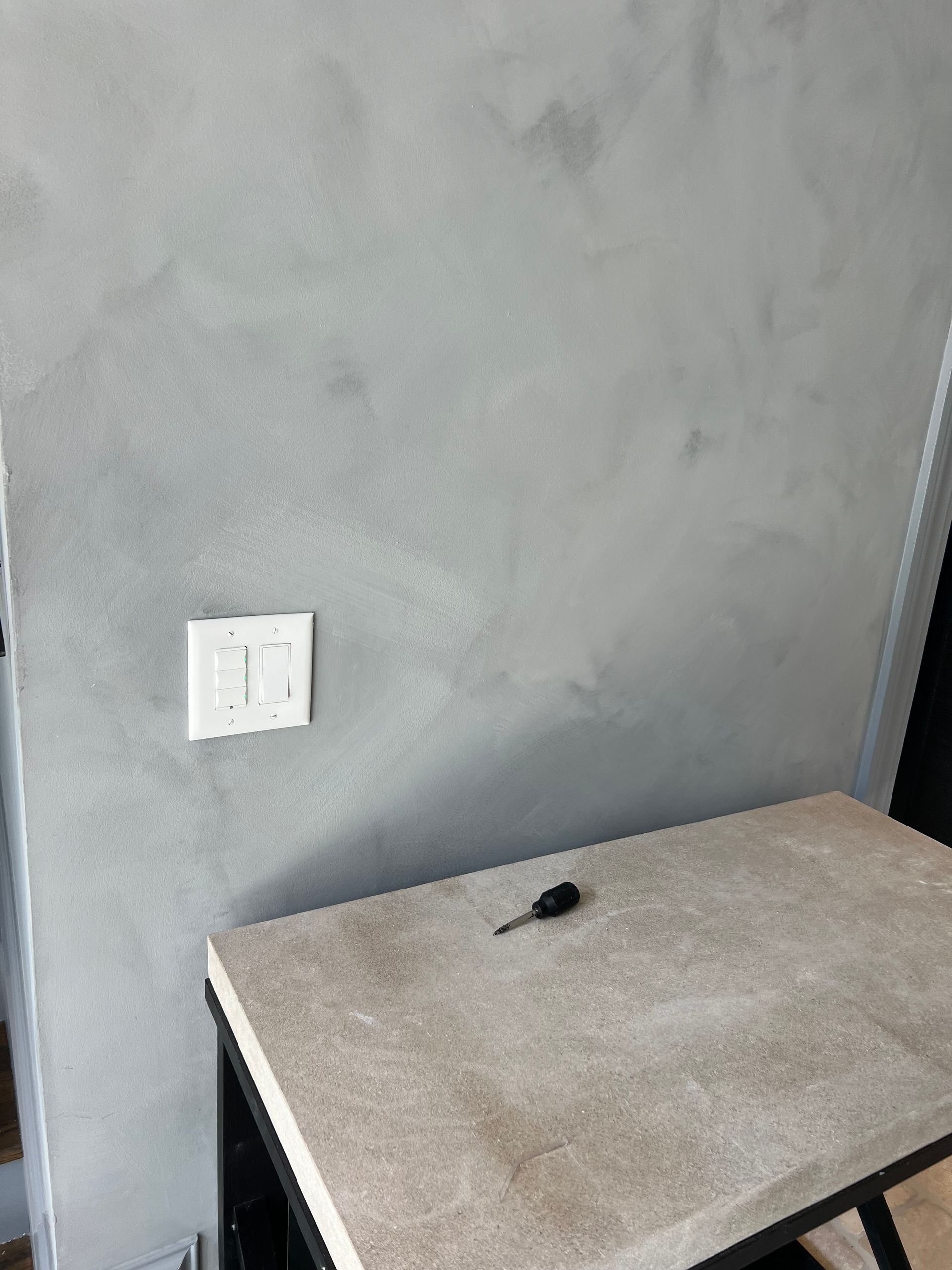 A table with a screwdriver on it in front of a gray wall.