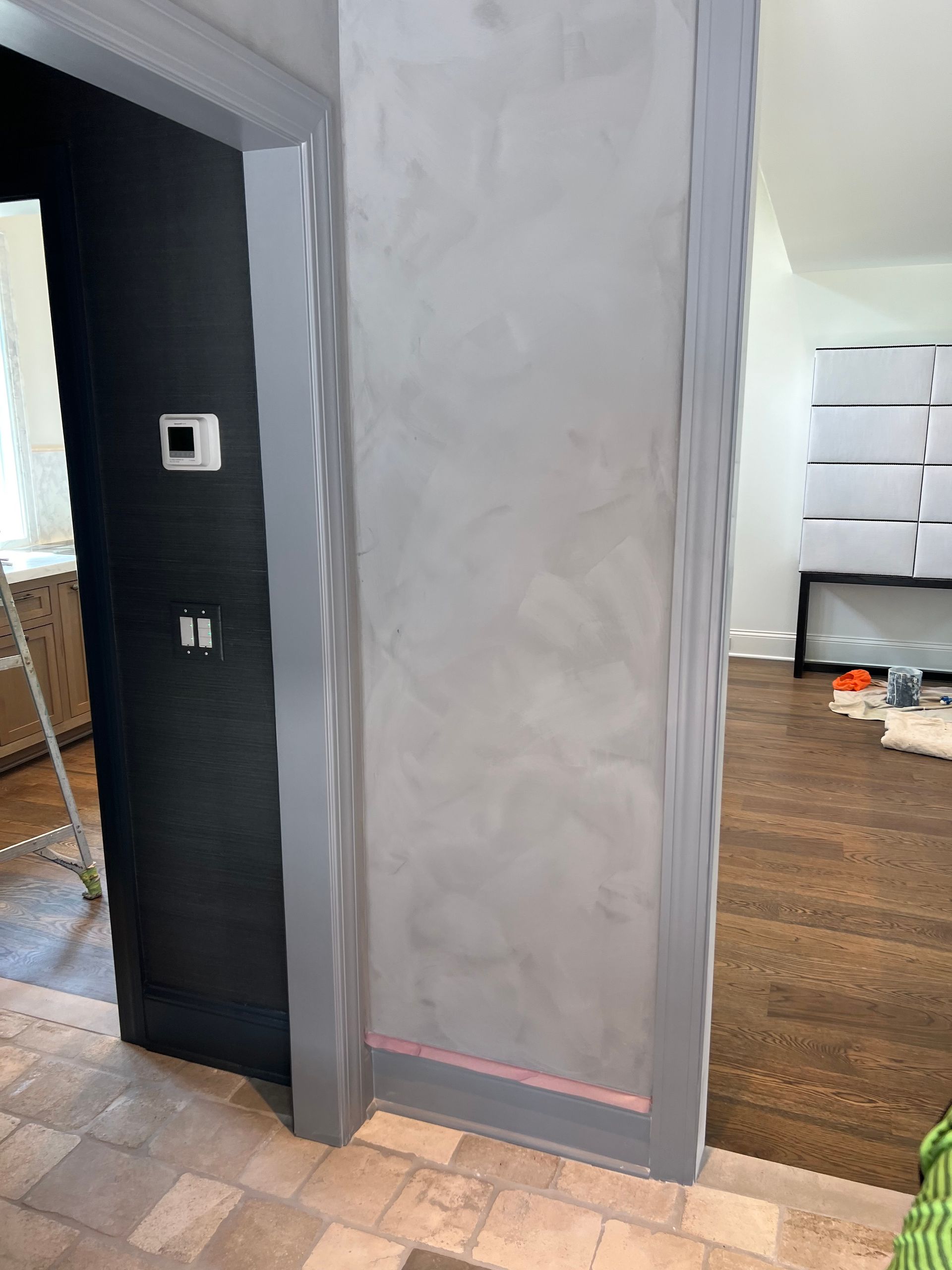 A corner of a room with a gray wall and a black door.