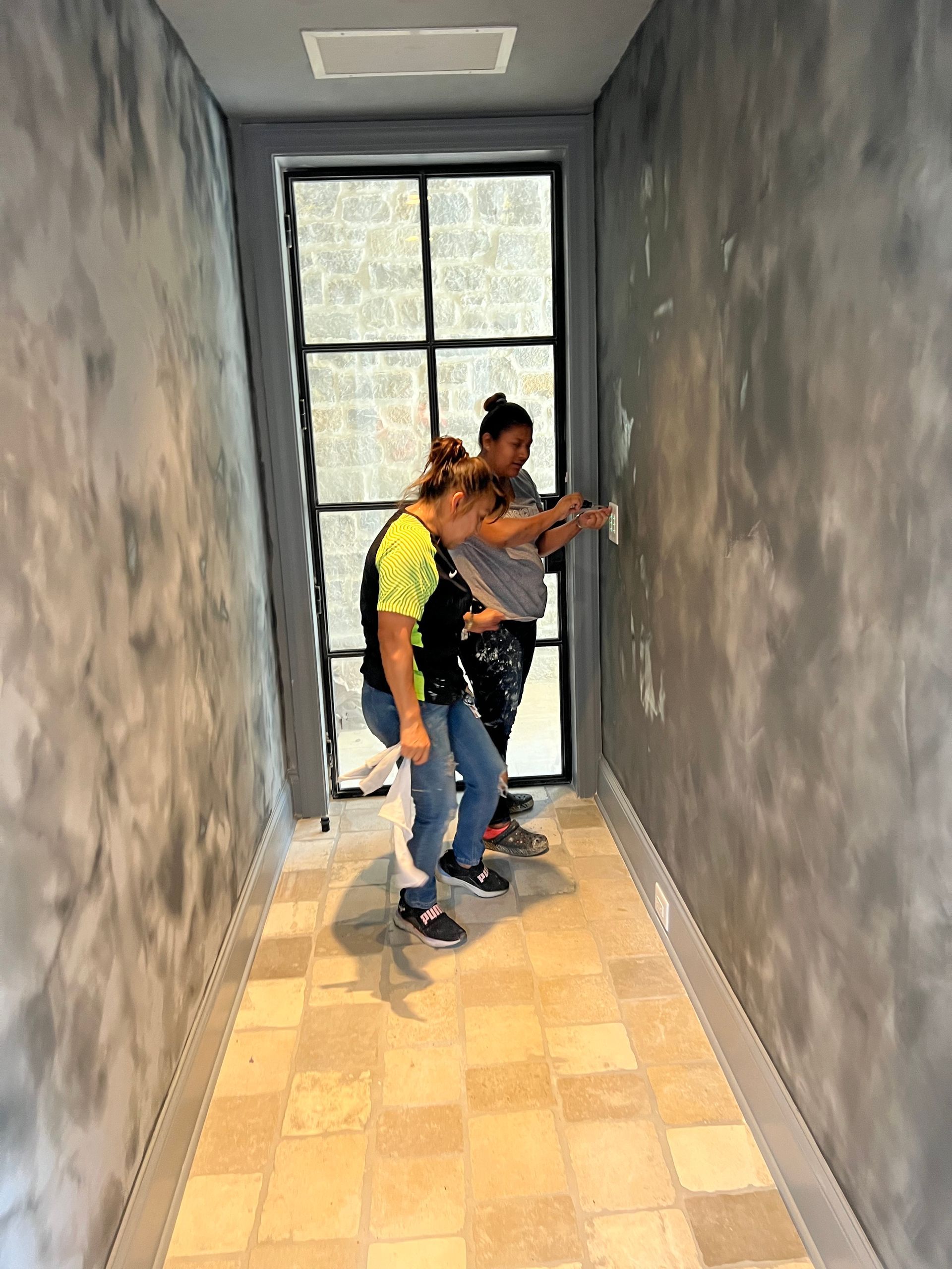 Two people are painting a wall in a hallway.
