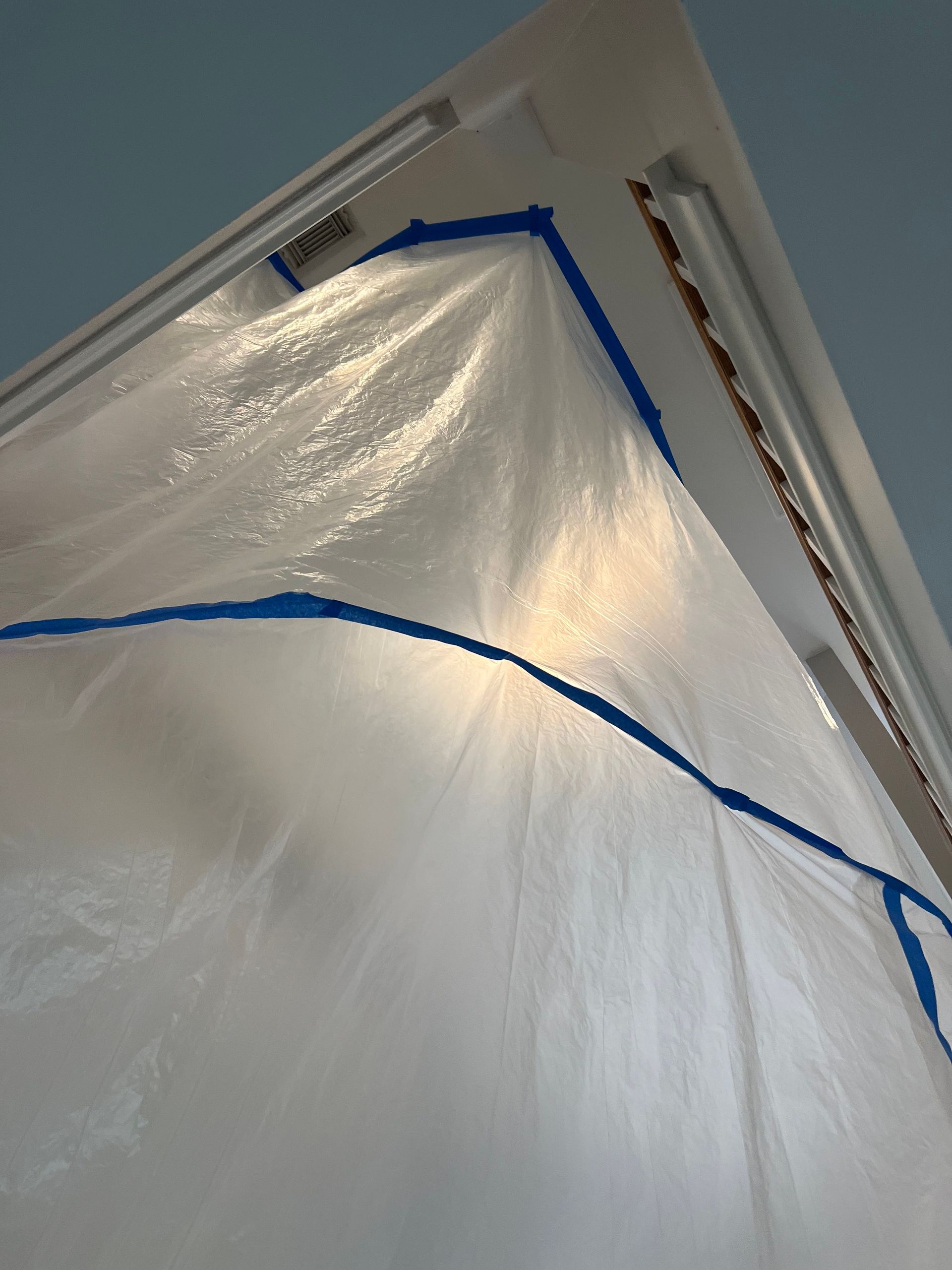 A white tarp is covering a door with blue tape