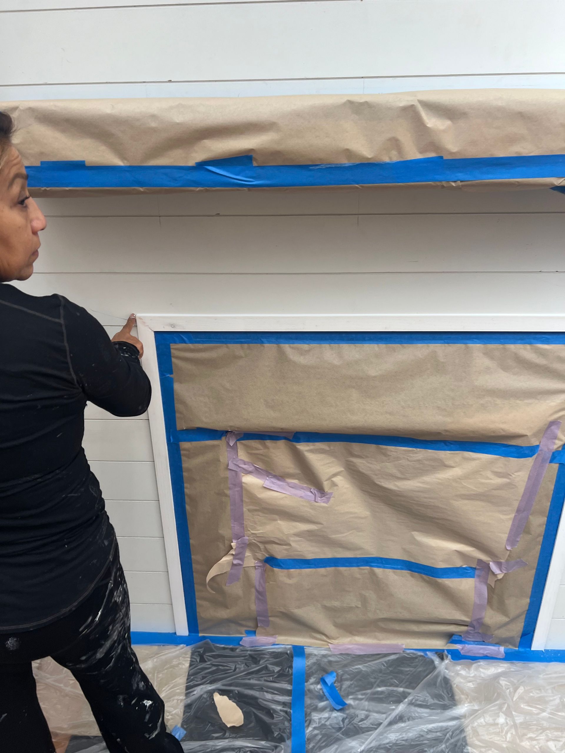 A woman is painting a wall with blue tape.