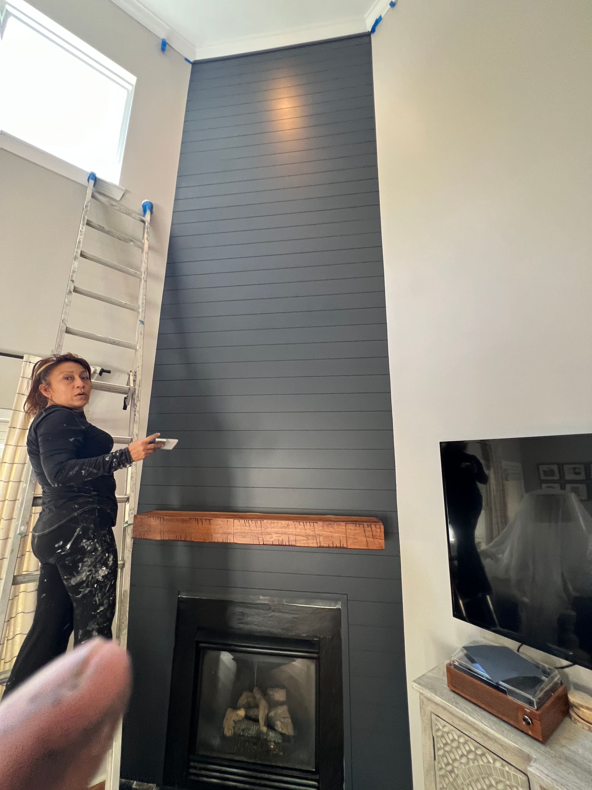 A woman is painting a fireplace in a living room.