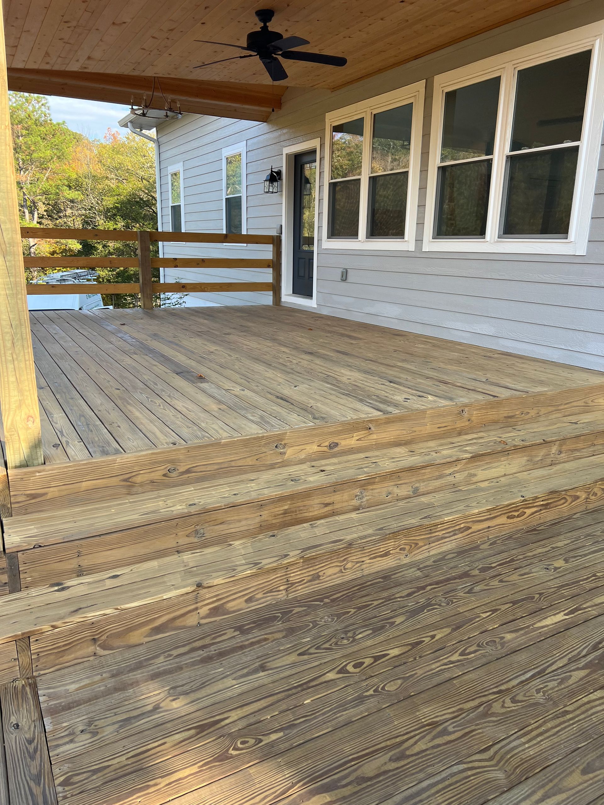 An empty porch with a ceiling fan and a wooden railing.