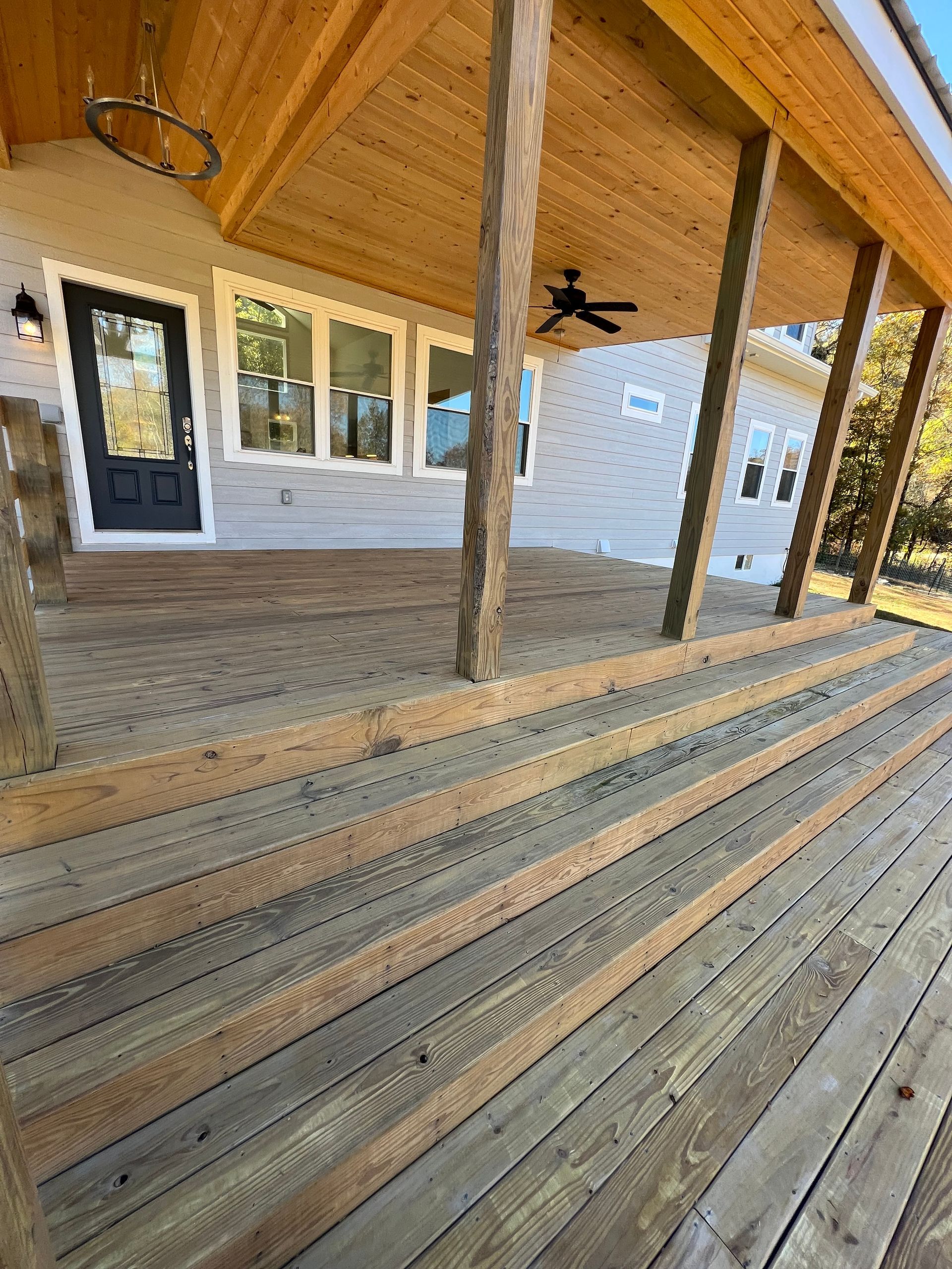A wooden deck with a ceiling fan and stairs leading to a house.