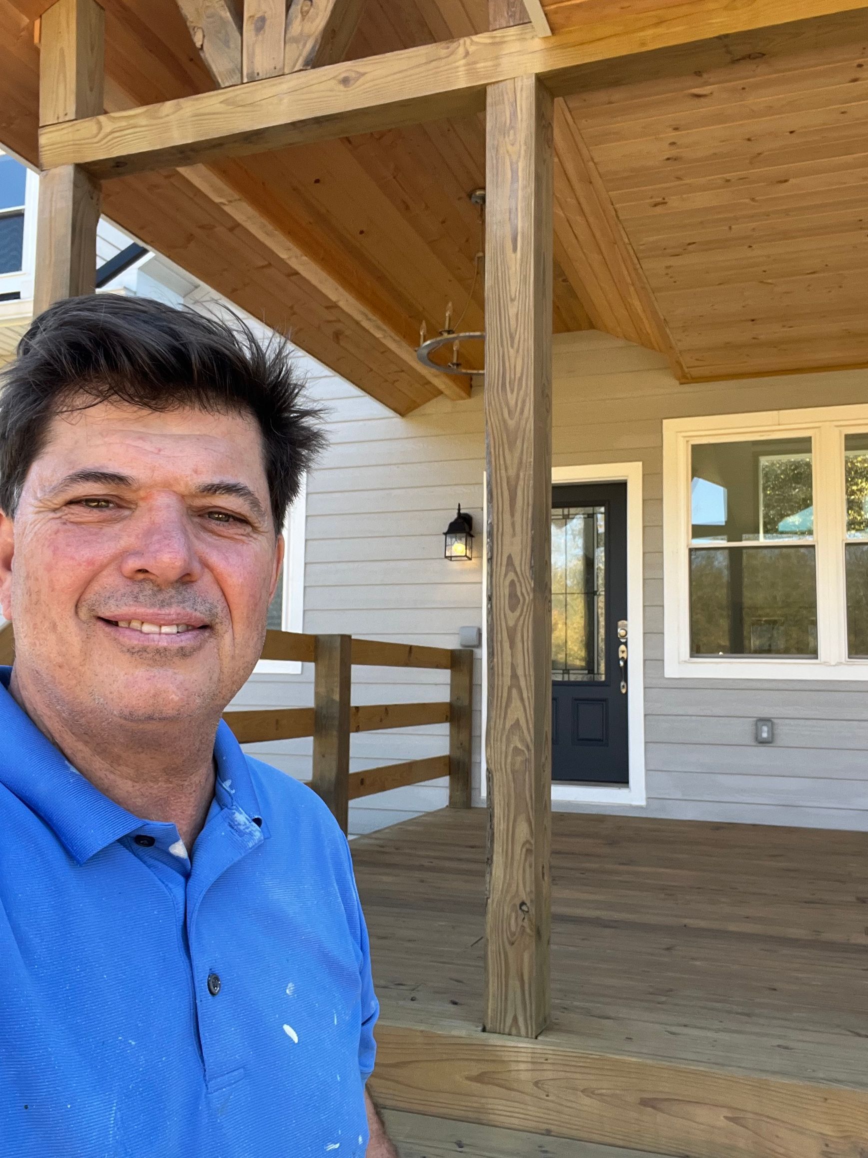 A man in a blue shirt is standing on a porch in front of a house.