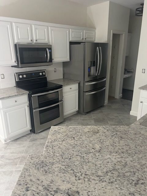 A kitchen with white cabinets , stainless steel appliances and granite counter tops.