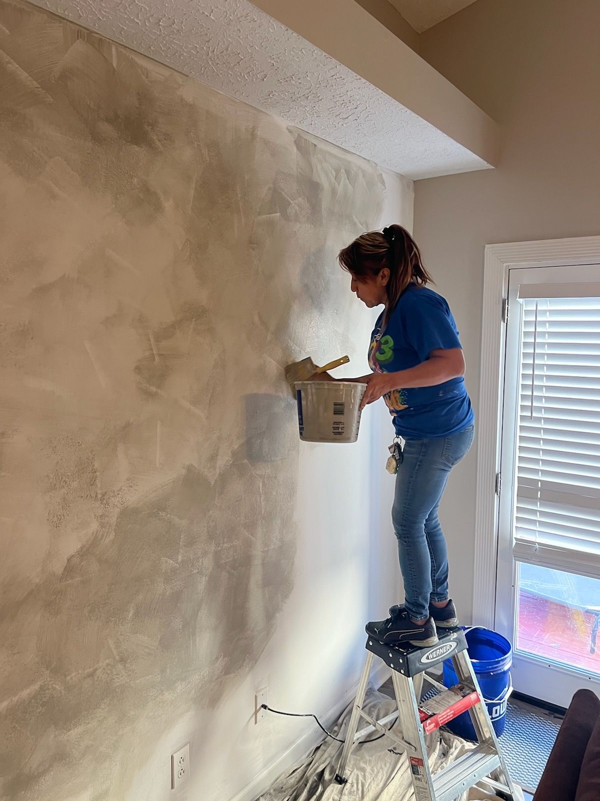A woman is standing on a ladder painting a wall.