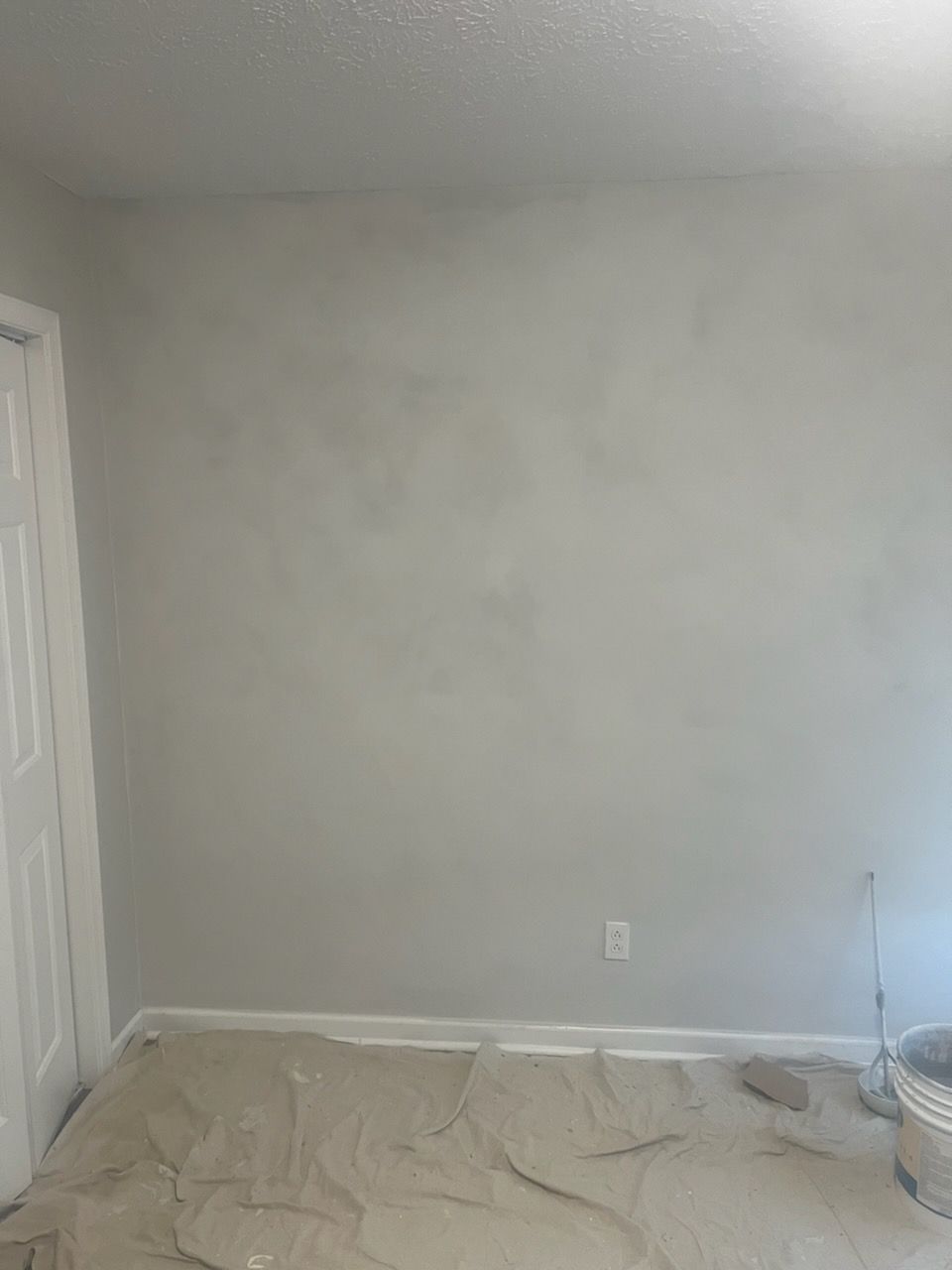 A room with a toilet and a bucket of paint on the floor.