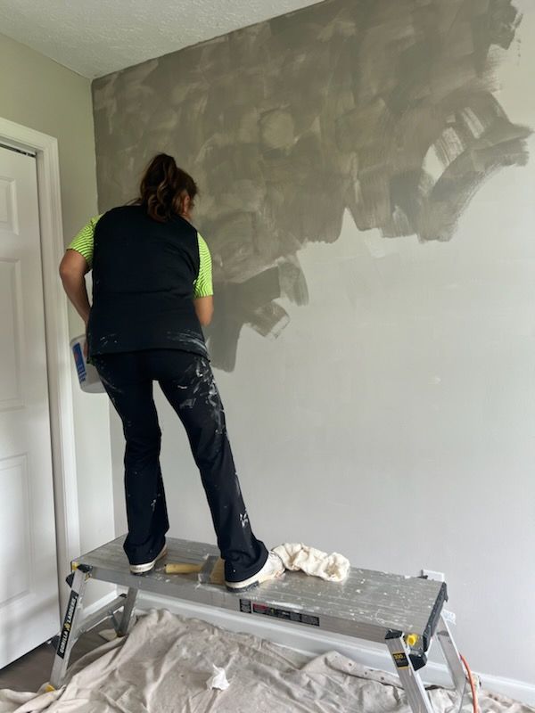 A woman is standing on a ladder painting a wall.