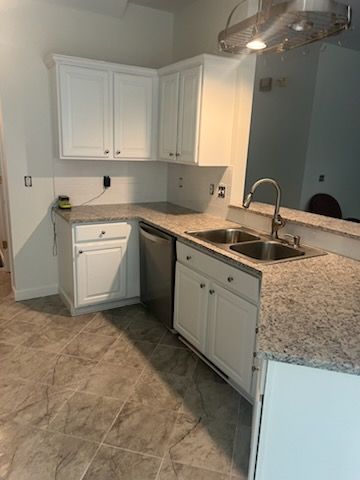 A kitchen with white cabinets , granite counter tops , a sink and a dishwasher.