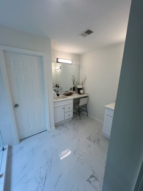 A bathroom with white cabinets and marble floors