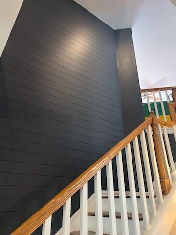 A staircase with a wooden railing and a black wall.
