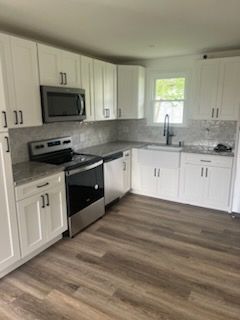 A kitchen with white cabinets , stainless steel appliances , a sink , and a microwave.