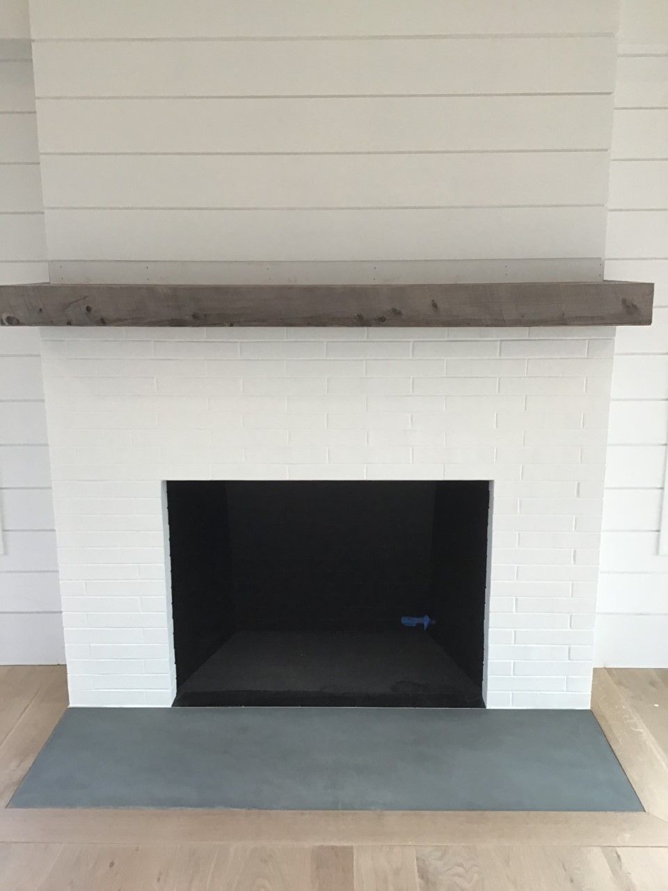 A white brick fireplace with a concrete mantle in a living room.