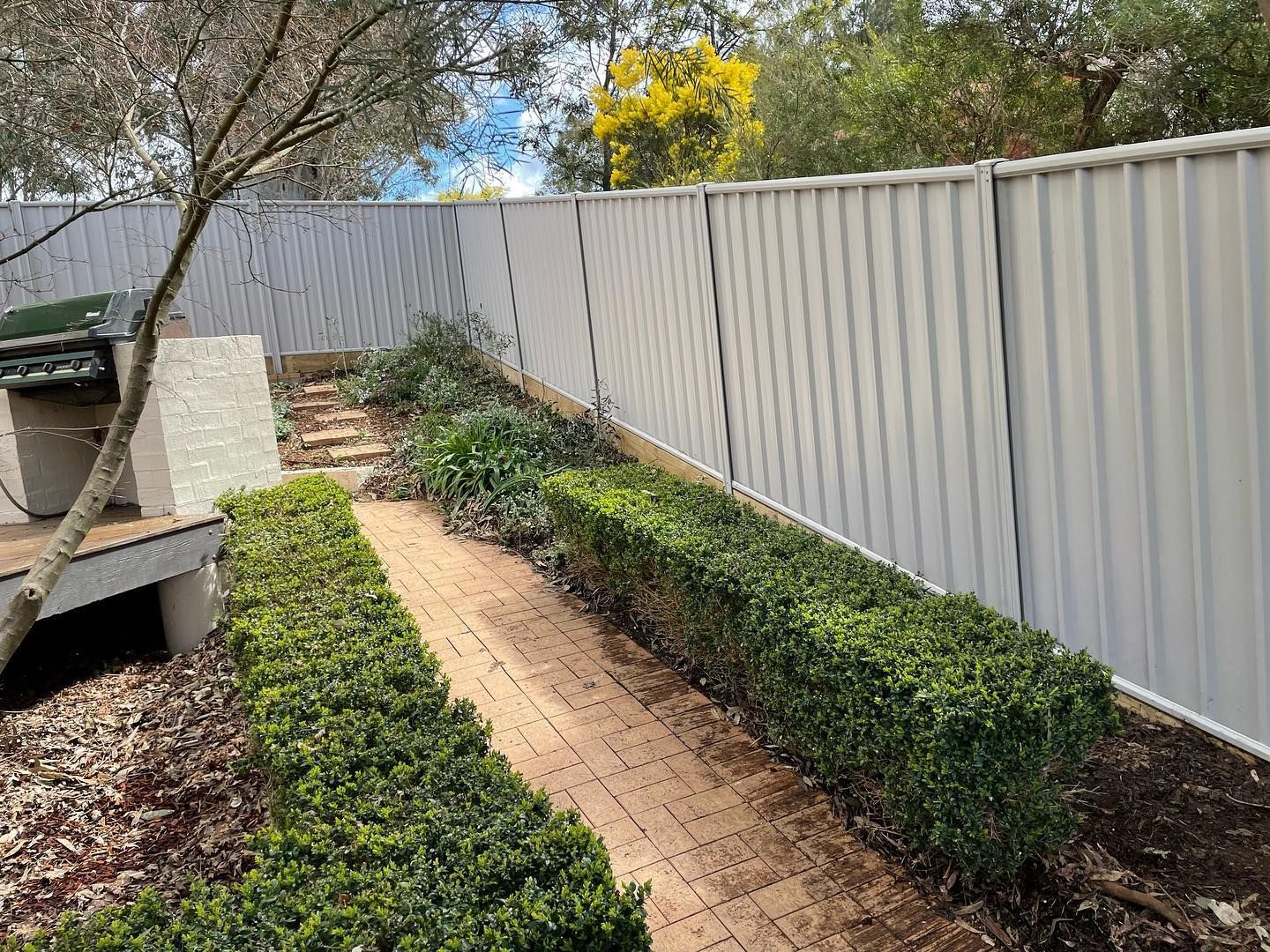 A white fence surrounds a brick walkway in a backyard.